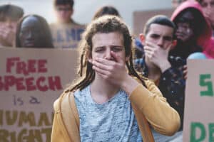 Students Protesting for Free Speech: Group outdoors, covering mouths, holding signs (e.g., "free speech is a human right"), with focus on blond teenager with dreadlocks.