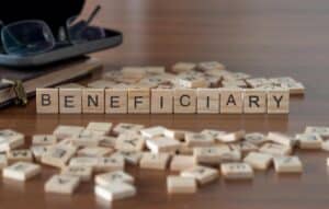 beneficiary word or concept represented by wooden letter tiles on a wooden table with glasses and a book