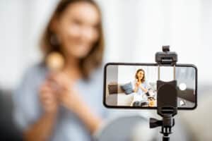 Young woman recording on a smart phone her vlog about cosmetics, showing and demonstrating makeup, close-up on phone. Influencer marketing in social media concept